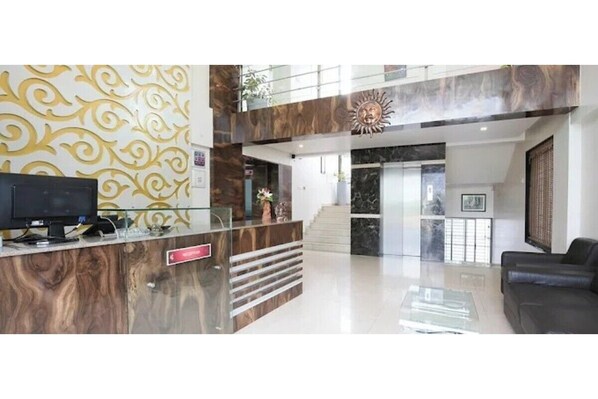 A reception area with a marble reception desk, a black leather sofa, and a staircase leading to an upper level. - Hotel Sunland (Baramati)