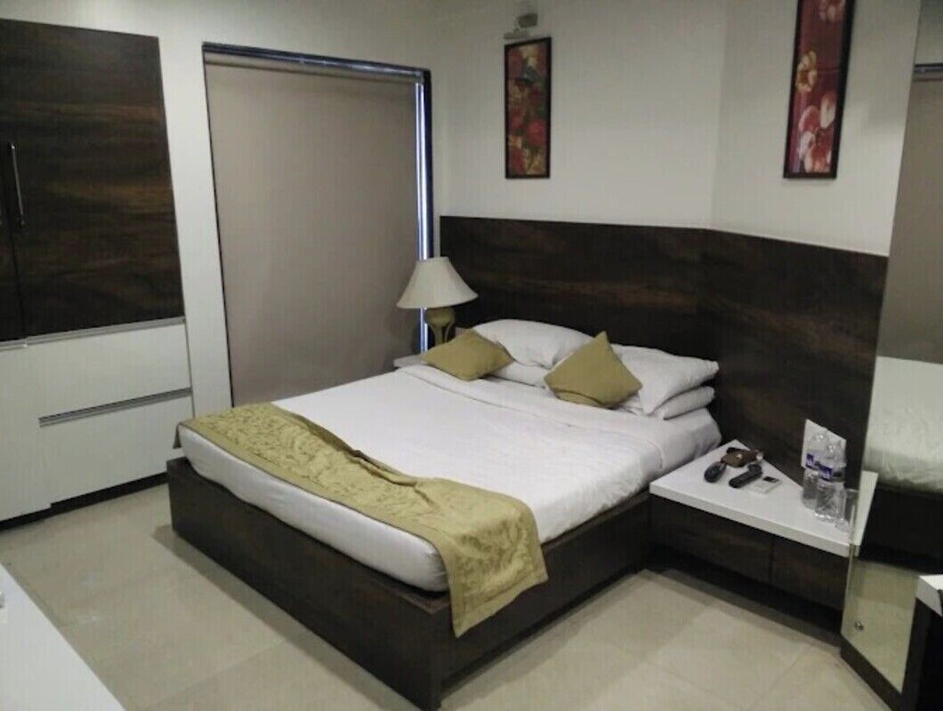 A hotel room with a large bed, a bedside table with a lamp, and a small table with a remote control and a glass of water.