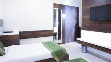 Ein Hotelzimmer mit zwei Betten, einem an der Wand montierten Fernseher, einem Holz-Kopfteil und einem kleinen Tisch mit einer Wasserflasche.