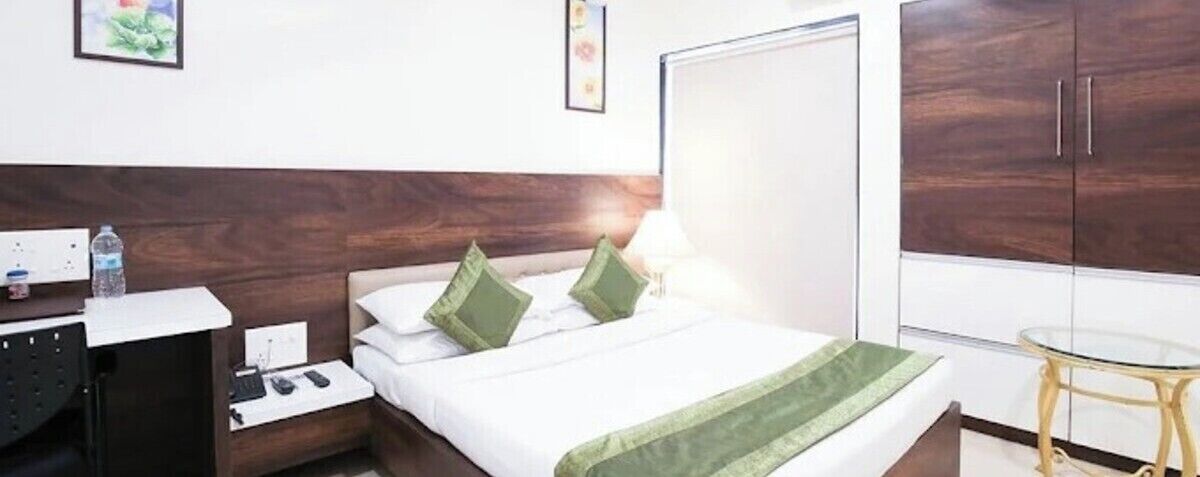 A hotel room with a bed, bedside table, lamp, wardrobe, and a small round table.