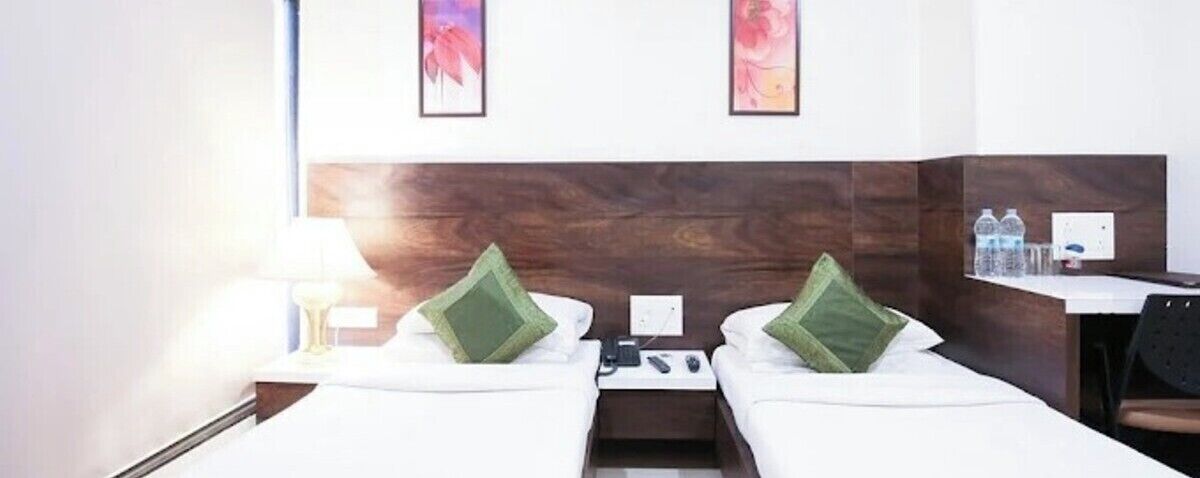Une chambre d’hôtel avec deux lits, une table de chevet avec une lampe, un bureau avec deux bouteilles d’eau et des œuvres d’art accrochées au mur.