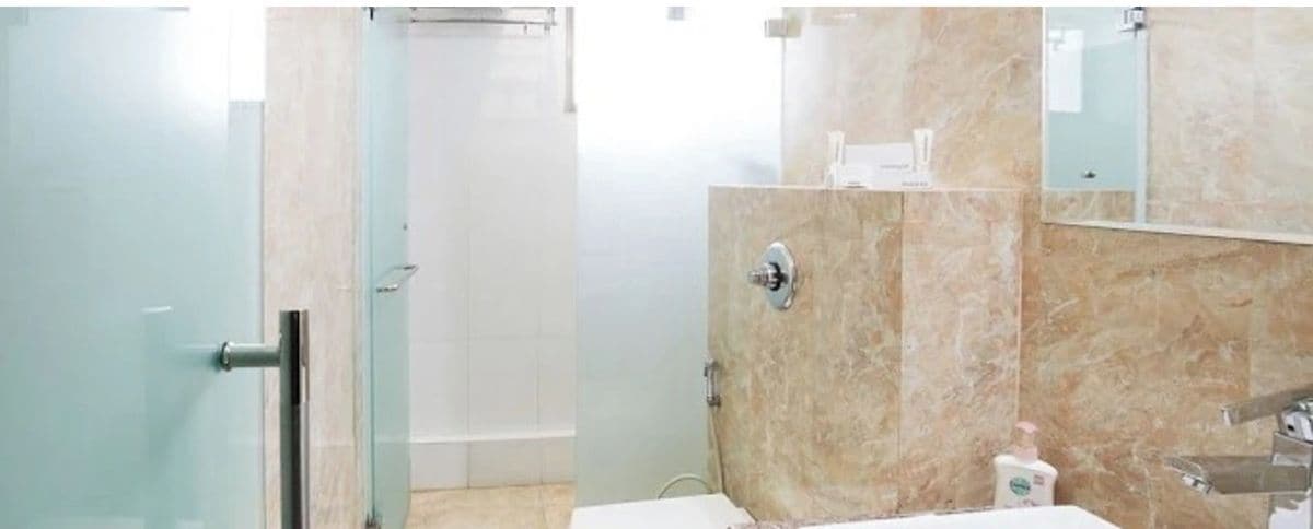 A bathroom with a glass shower door, a marble wall, a sink, and a mirror.