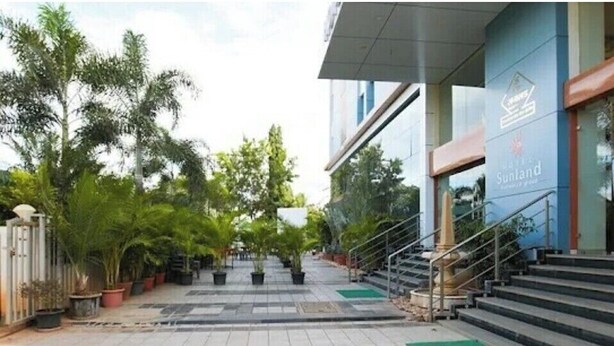 A modern building with a staircase leading to a glass entrance. - Hotel Sunland (Baramati)