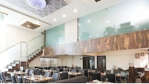A spacious dining area with multiple tables and chairs, a staircase, and a modern interior design. - Hotel Sunland (Baramati)