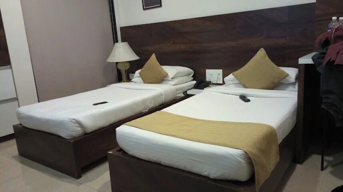 Two single beds with wooden headboards, a bedside table with a lamp, and a wall-mounted phone.