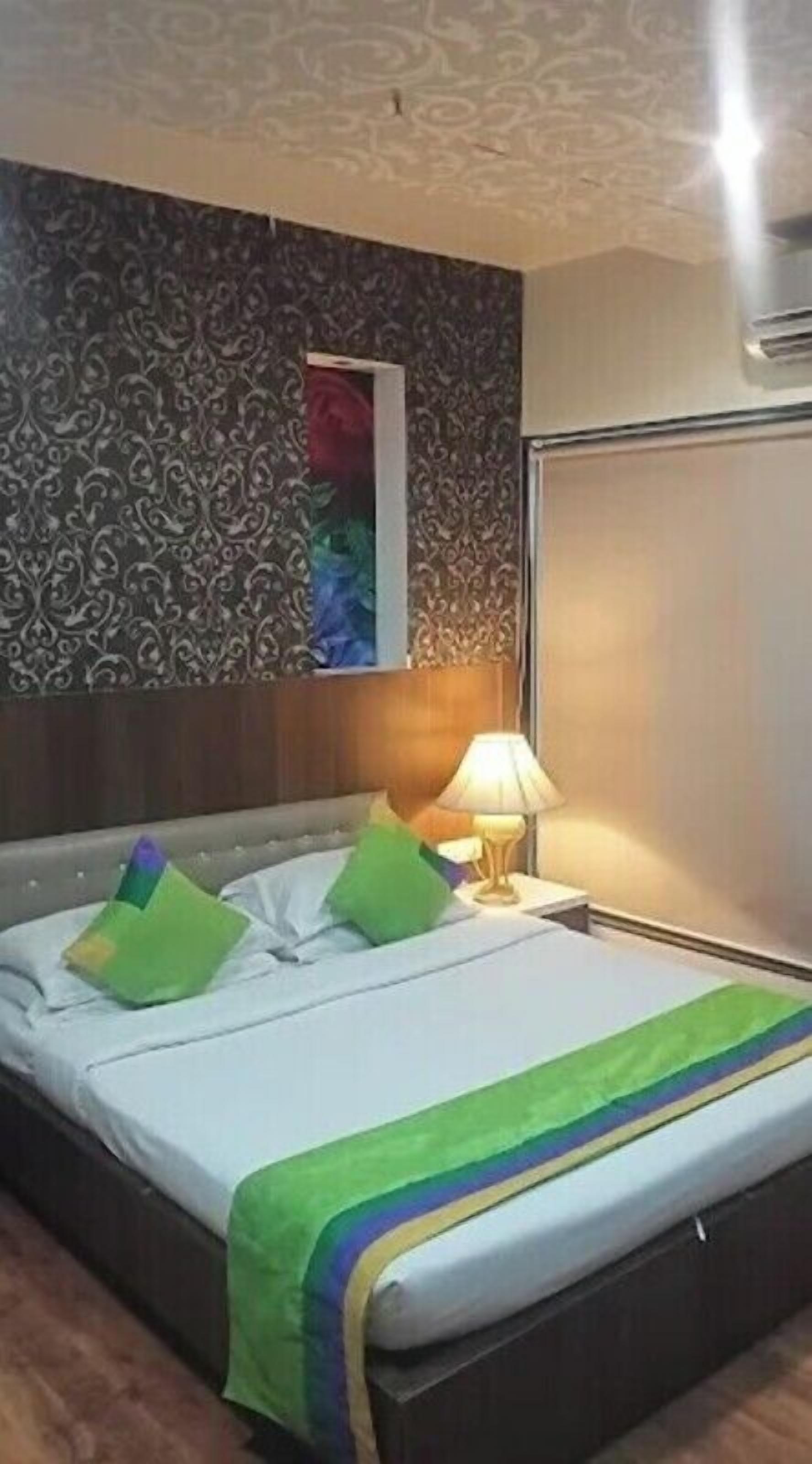 A neatly made bed with a green and blue striped blanket, a wooden headboard, and a patterned wall.