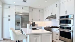 Une cuisine moderne avec des meubles blancs, des appareils en acier inoxydable et un îlot central doté de tabourets de bar.