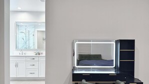 Une chambre à coucher moderne, dotée d’une coiffeuse, d’un lit avec une tête de lit et d’un grand miroir.