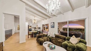 A modern living room with a large sectional sofa, a white coffee table, and a view of the sunset through large windows.
