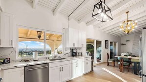 A modern kitchen with white cabinetry, stainless steel appliances, and a large window offering a view of the outdoors.