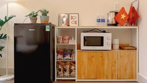Eine kompakte Küchenzeile mit einem Kühlschrank von Hisense, einer Mikrowelle, einem Holzschrank und einer kleinen Ablage mit verschiedenen Gegenständen, darunter ein Wasserspender, ein Wasserkocher und einige Flaggen.