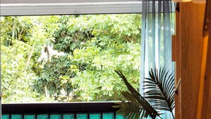 A dining area with a table and chairs, a view of greenery outside, and a patterned wall. - Ti Cosy Gosier Swimming pool & beach (Le Gosier)