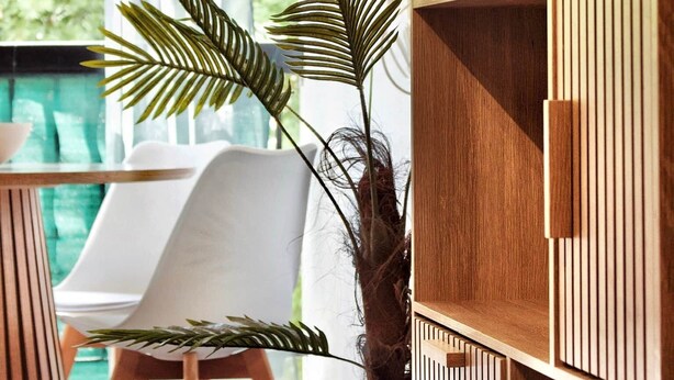 A modern room with a wooden cabinet, a white chair, and a large plant. - Ti Cosy Gosier Swimming pool & beach (Le Gosier)