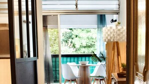 A modern interior with a sliding door leading to a balcony, a dining area with a table and chairs, and a painting on a easel. - Ti Cosy Gosier Swimming pool & beach (Le Gosier)