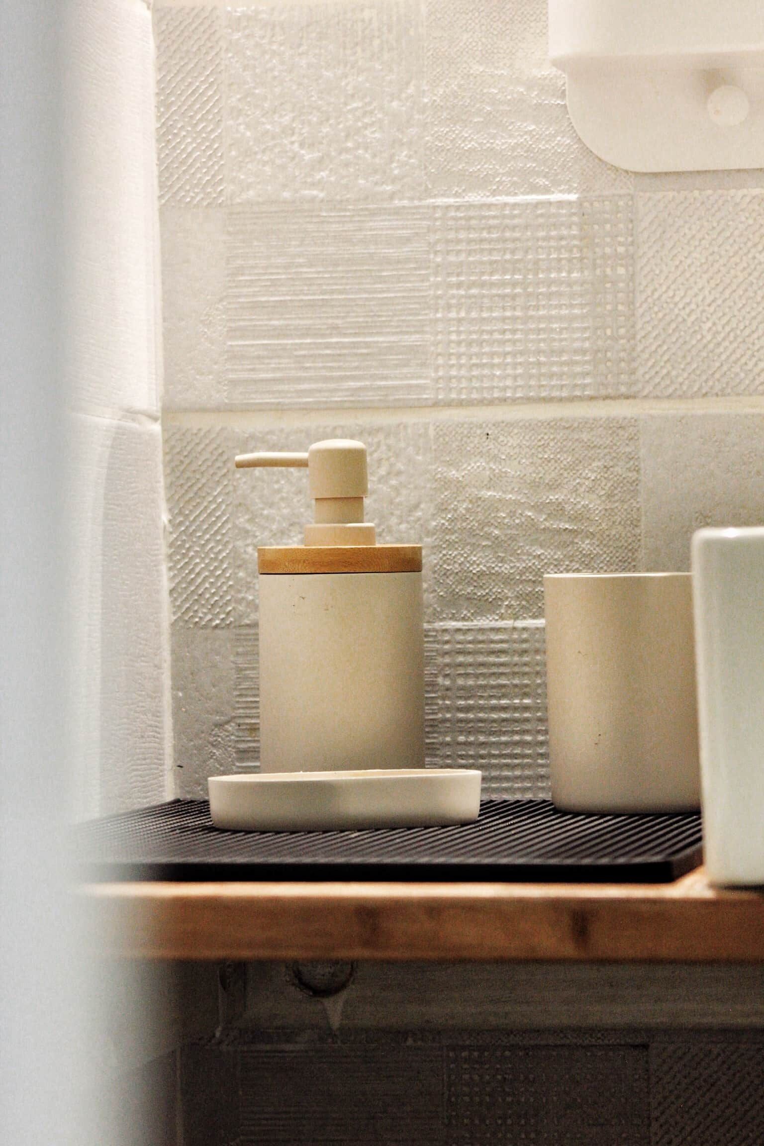 A bathroom with a wooden shelf holding a soap dispenser, a small dish, and a cup.