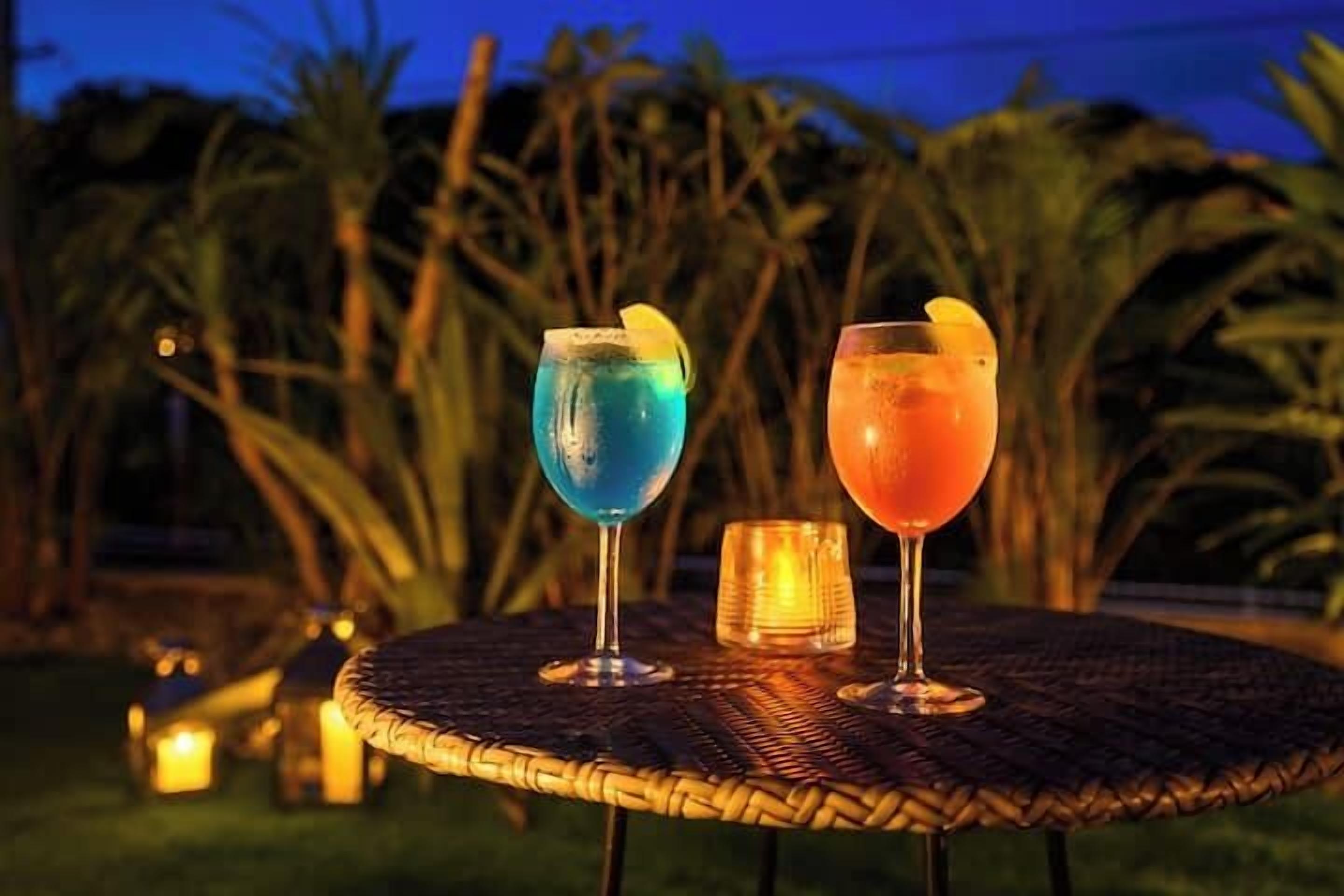 Two drinks on a wicker table outdoors at dusk with palm trees in the background.