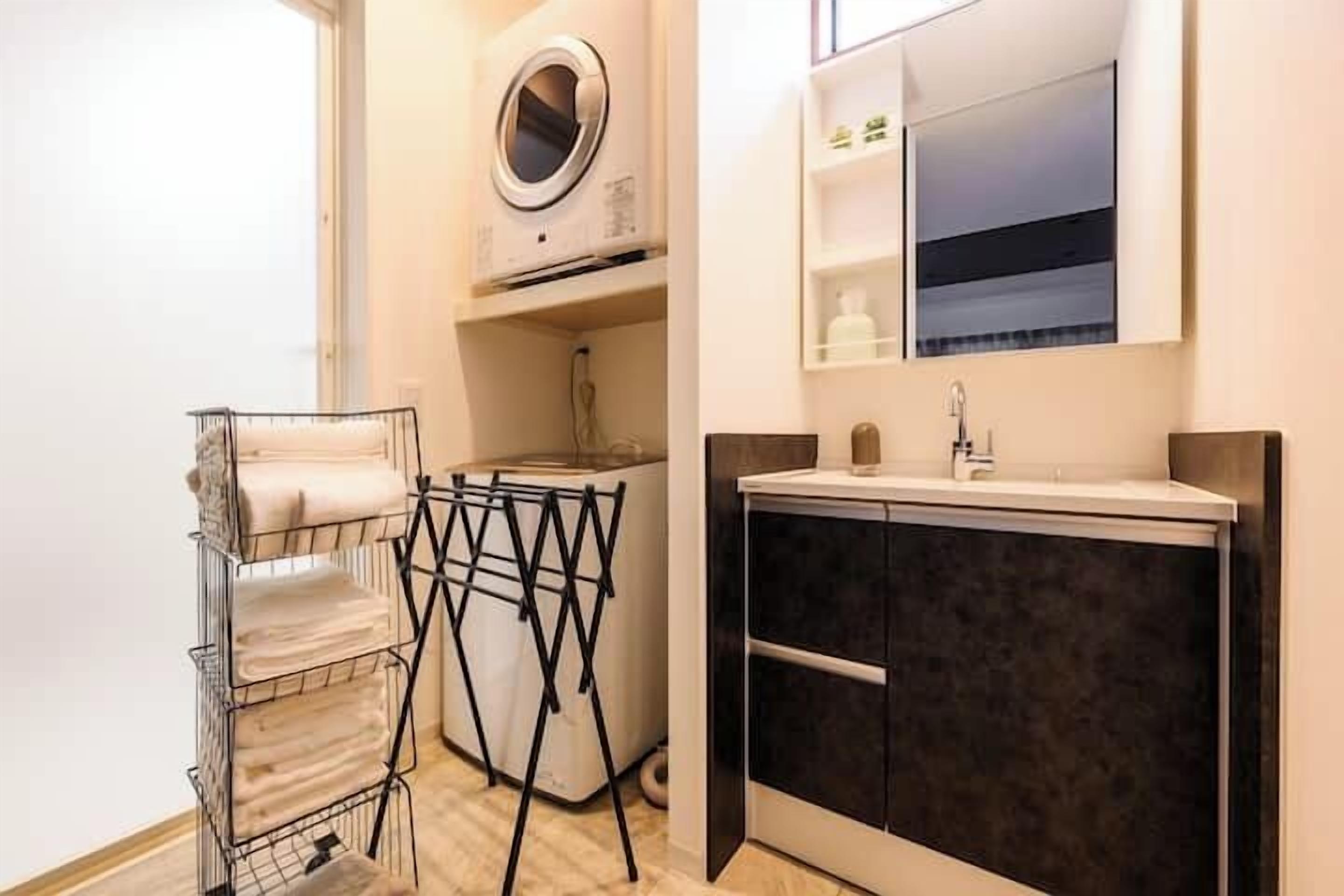 A compact bathroom with a built-in washing machine, a drying rack, and a modern vanity with a mirror and shelves.