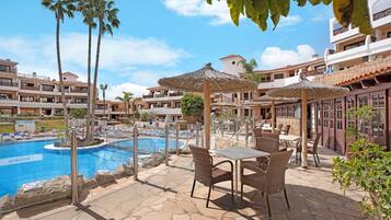 Área de piscina en un resort con mobiliario exterior y palmeras.