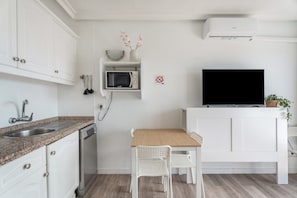 A compact kitchen with white cabinetry, a microwave, a sink, a wooden table with two chairs, a television, and a small plant.