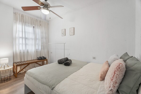 A bedroom with a bed, a wooden bench, a desk with a lamp, and a ceiling fan.
