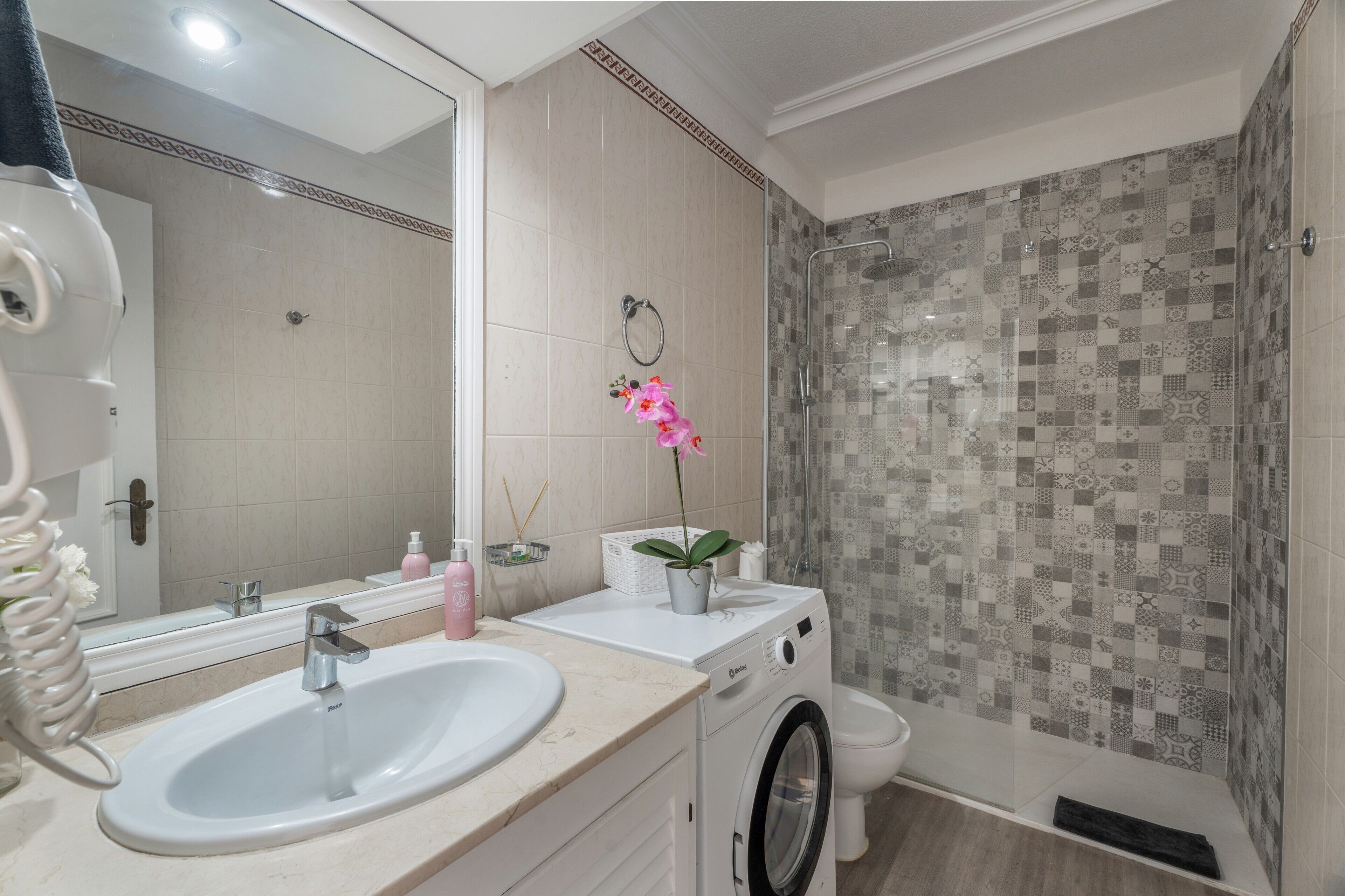 Une salle de bain équipée d’un lavabo, d’un miroir, de toilettes et d’une douche dont les carreaux sont décorés de motifs.