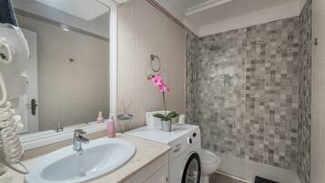 Une salle de bain équipée d’un lavabo, d’un miroir, de toilettes et d’une douche dont les carreaux sont décorés de motifs.