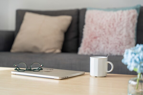 Una computadora portátil, una taza blanca y un par de lentes sobre una mesa de madera.