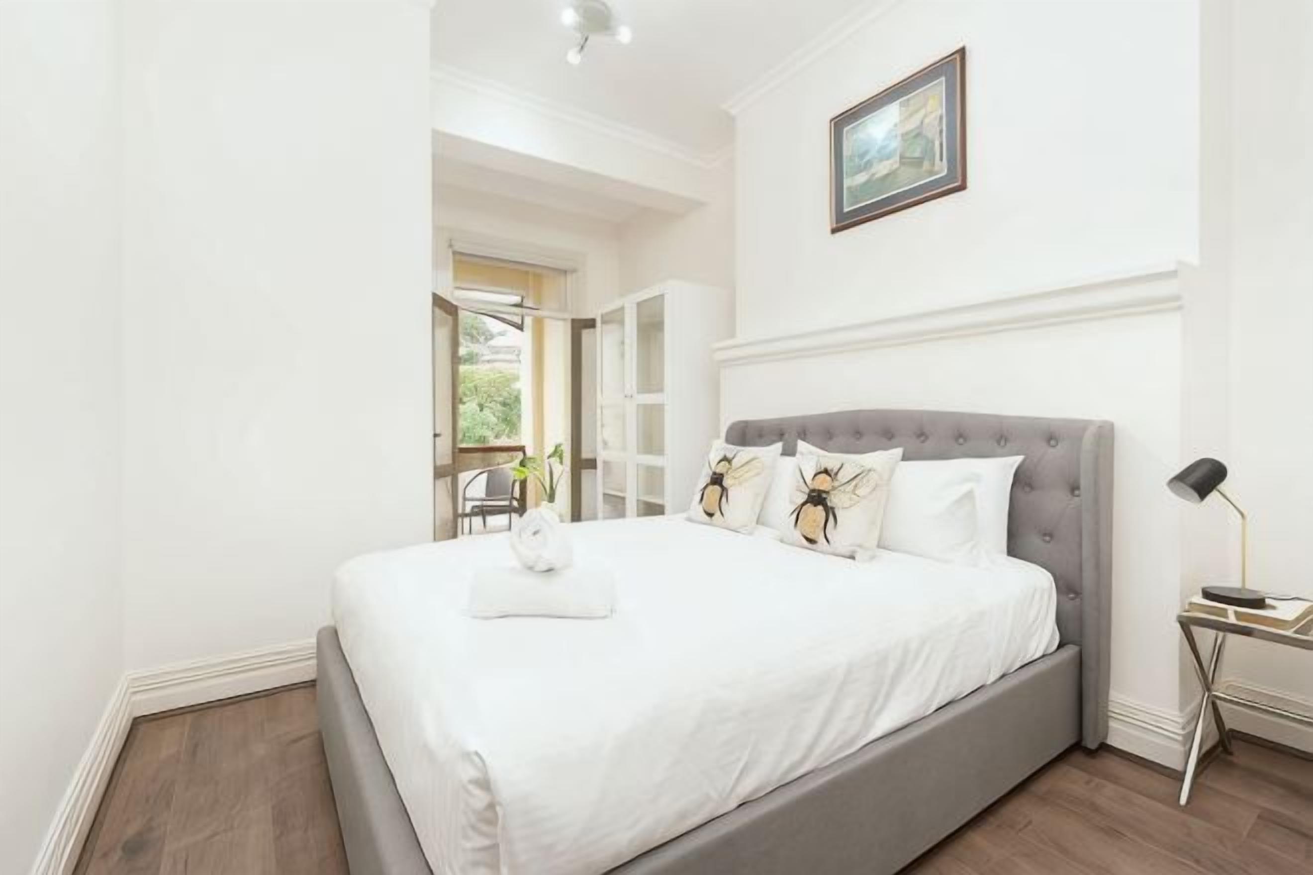 Un dormitorio con cama, mesita de noche, lámpara y vistas al exterior.