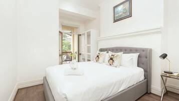 Un dormitorio con cama, mesita de noche, lámpara y vistas al exterior.