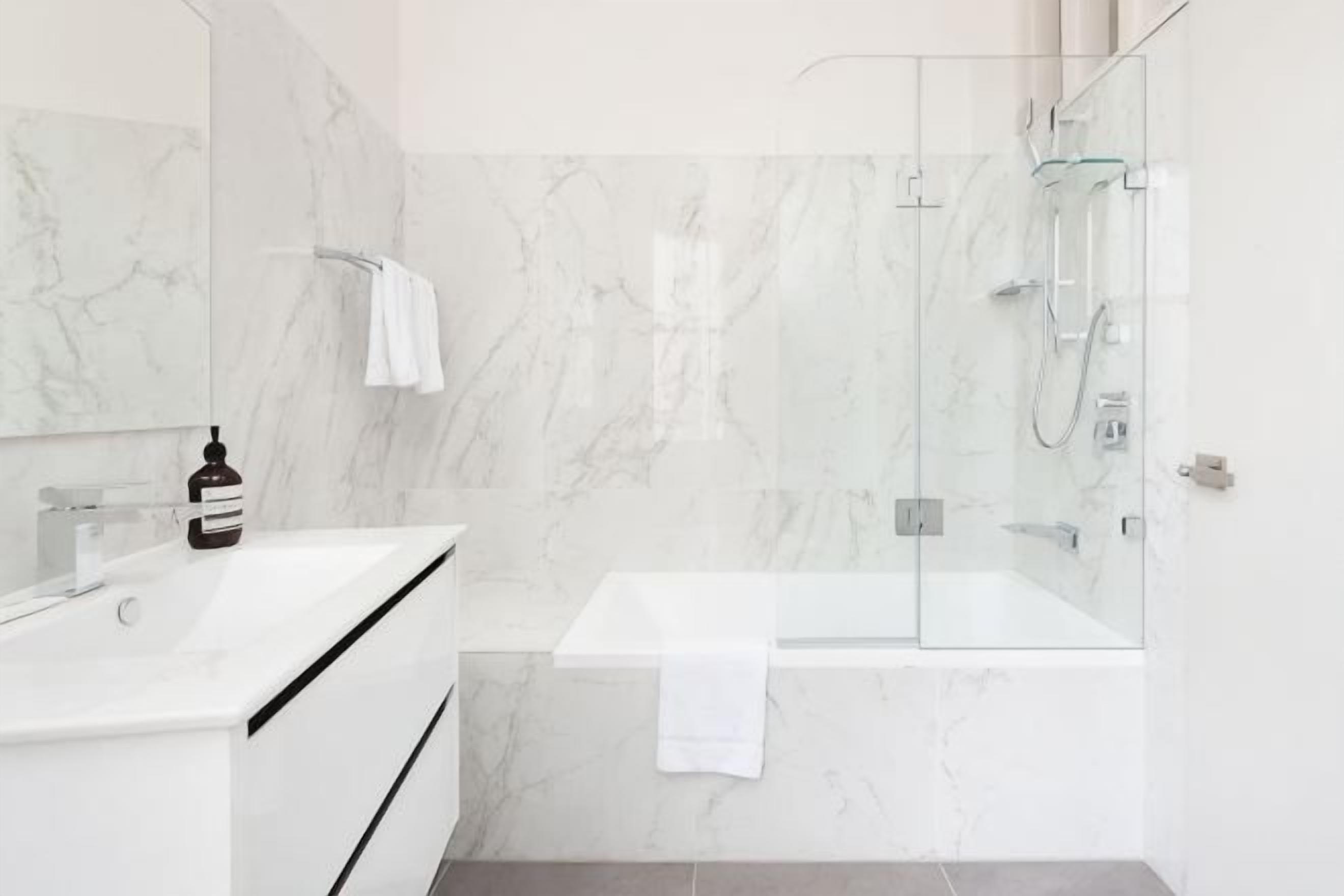 Un baño moderno con ducha de vidrio, lavamanos blanco y paredes de mármol.