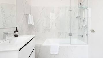 Un baño moderno con ducha de vidrio, lavamanos blanco y paredes de mármol.