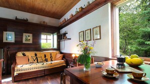 A cozy room with a wooden sofa, a dining table with a coffee maker, and a window overlooking greenery. - Beautiful  villa for 6 guests with WIFI, TV, terrace and pets allowed (Nevegal)