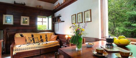 Una habitación acogedora con un sofá de madera, una mesa de comedor con una cafetera y una ventana con vistas a la vegetación.