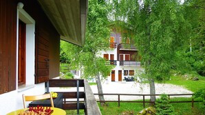 A wooden deck with a chessboard and a chair, overlooking a white building with a balcony, surrounded by greenery. - Beautiful  villa for 6 guests with WIFI, TV, terrace and pets allowed (Nevegal)