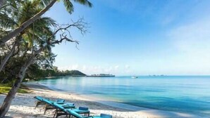 A beach with clear blue water, a sandy shore, and a row of blue lounge chairs. - Villa Waimarie | Lipa Noi Beachfront 6BR Villa — Pool & Chef (Surat Thani)