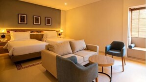 A hotel room with a bed, two sofas, a chair, a small table, and a window with blinds. - Montana Oceanside Mandalika (Central Lombok Regency)