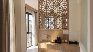 A hotel room with a wooden desk, a blue chair, a decorative screen, and a window with curtains. - Montana Oceanside Mandalika (Central Lombok Regency)