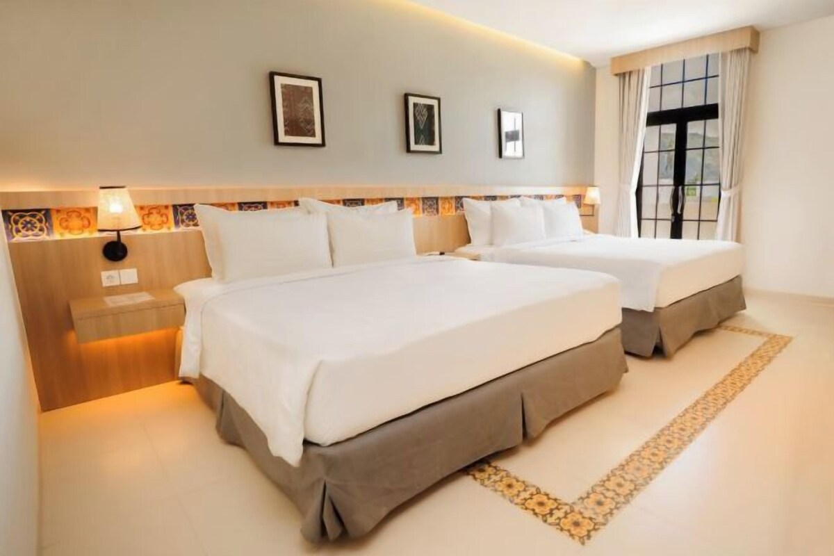 Een hotelkamer met twee bedden, een nachtkastje, een lamp en een raam met gordijnen.