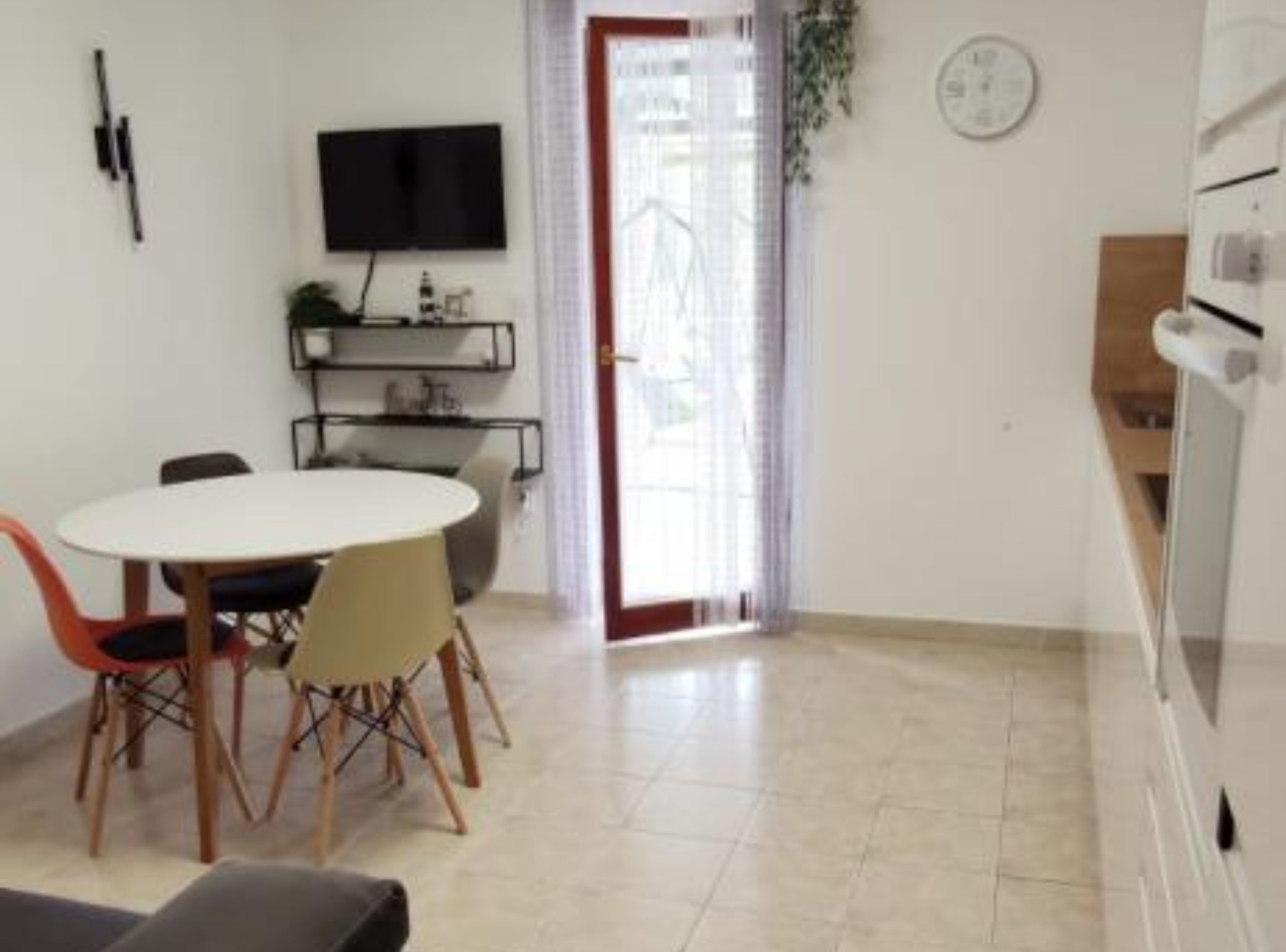 Een moderne keuken met een ingebouwde oven, een eethoek met een ronde tafel en stoelen, en een aan de muur bevestigde televisie.