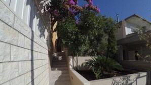 A narrow pathway leading to a building with a stone wall on one side and a concrete planter with plants on the other. - Apartments Maritimo (Smokvica)