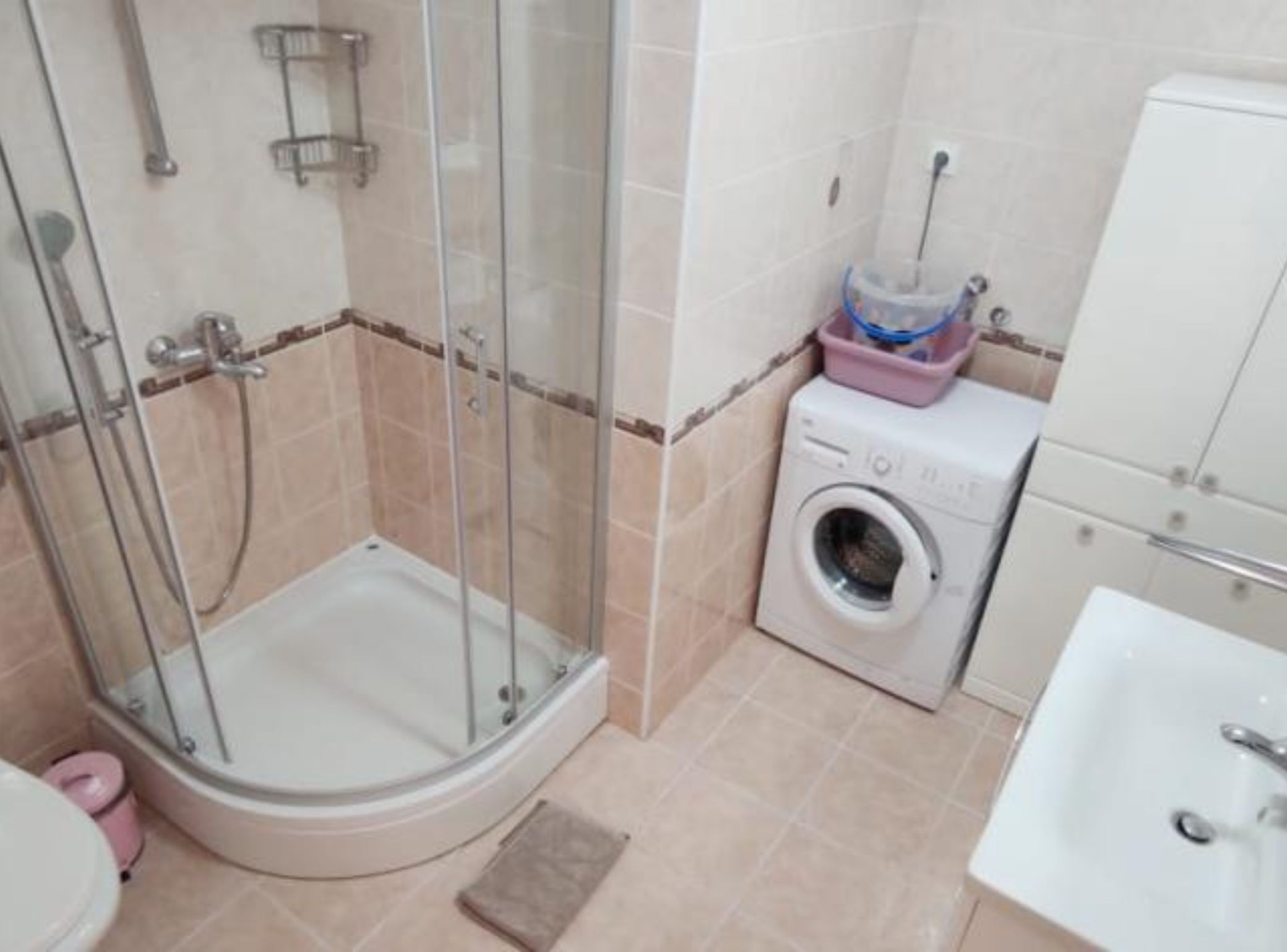 A bathroom with a glass-enclosed shower, a washing machine, and a sink.