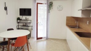 A compact kitchen with a dining area, a TV mounted on the wall, and a window with curtains. - Apartments Maritimo (Smokvica)