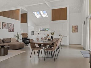 A modern interior with a dining area, kitchen, and living space, featuring a high ceiling and skylights.