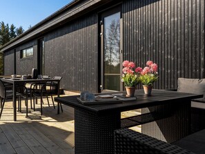 A modern outdoor patio with a dining table, chairs, and potted flowers.