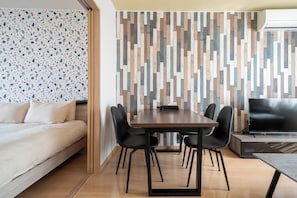 A modern room with a bed, a dining table with chairs, a TV, and a patterned wall. - LAMBRUSCO (Kamifurano)