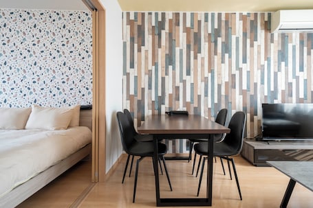 A modern room with a bed, a dining table with chairs, a TV, and a patterned wall.