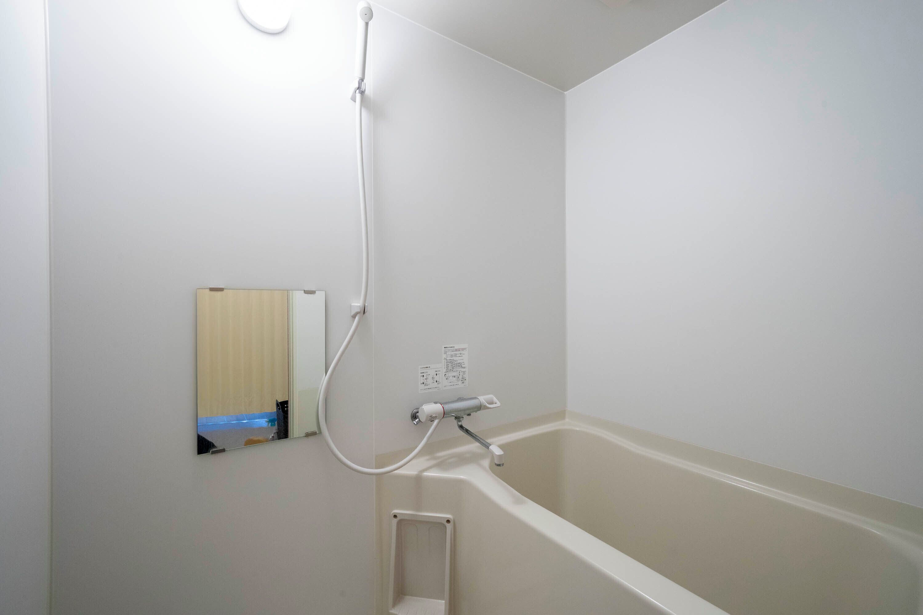 Un baño con bañera, ducha y un espejo pequeño.