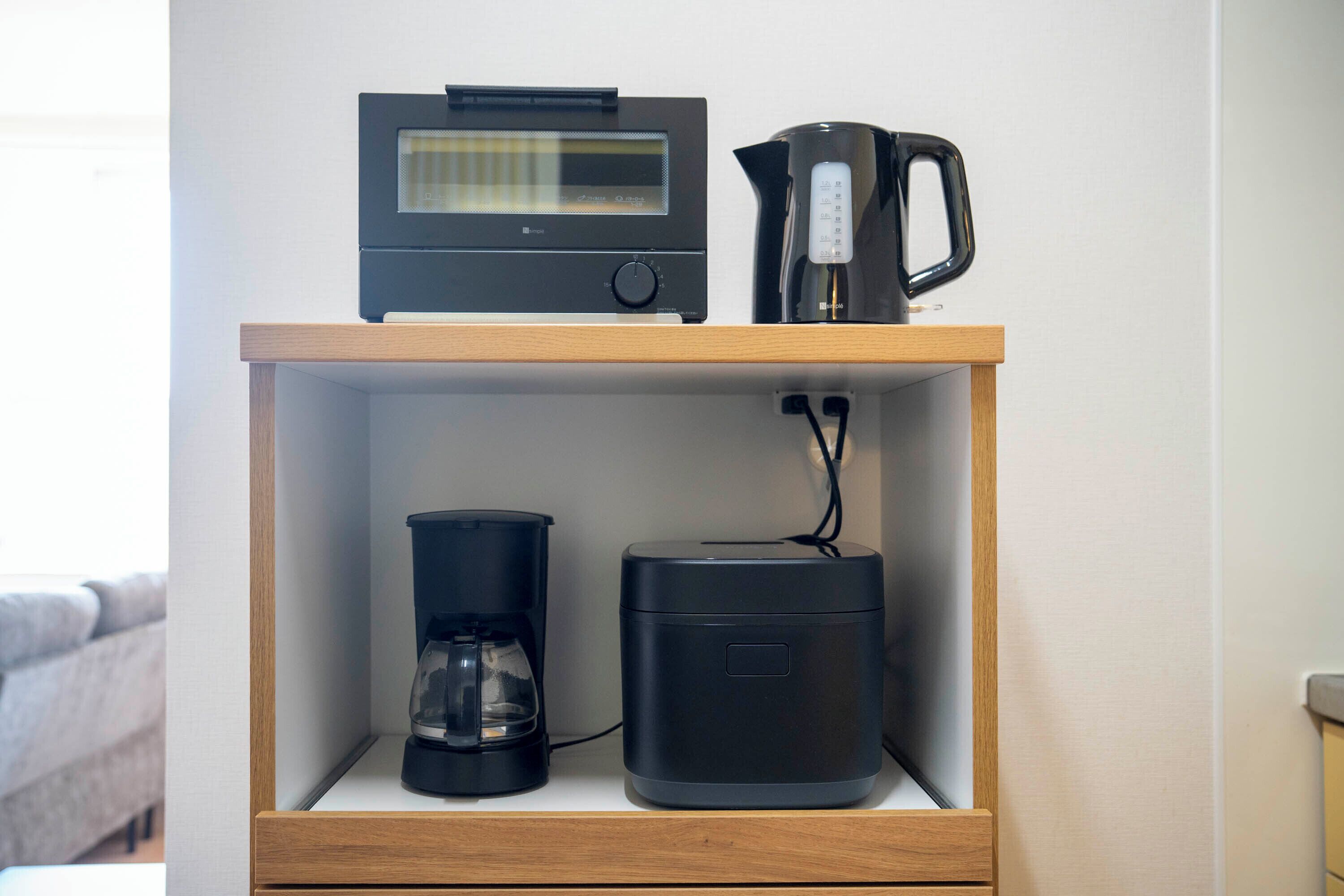 Une étagère en bois sur laquelle se trouvent une machine à café noire, une cafetière noire et un appareil électronique noir.