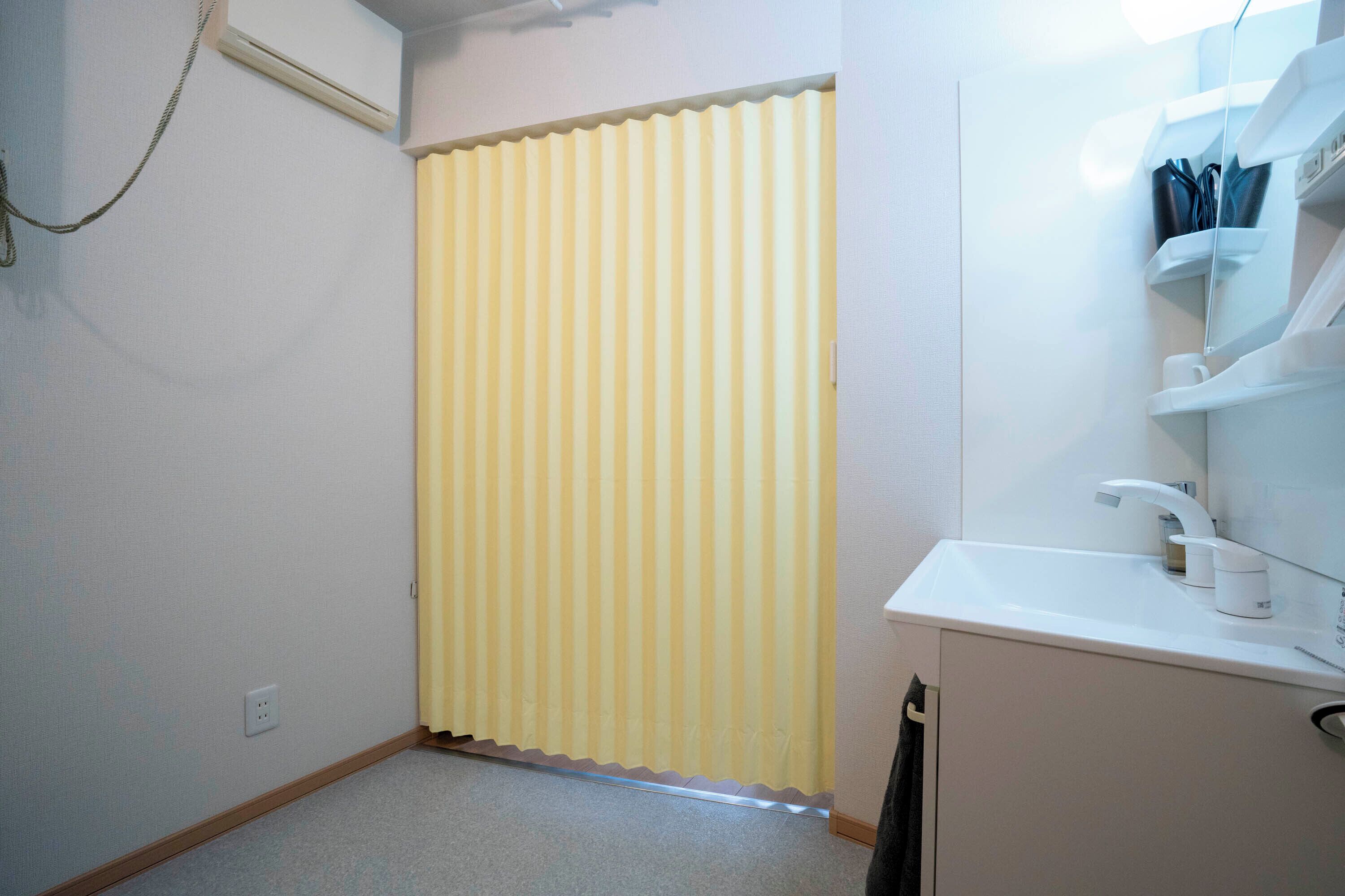 Baño pequeño con inodoro, lavamanos y espejo. La puerta tiene una cortina amarilla a rayas.