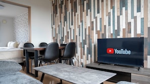 Una habitación de hotel moderna con un panel de madera, un televisor de pantalla plana, un rincón de comedor con sillas y un sofá.